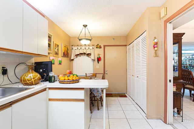 kitchen with hanging light fixtures, backsplash, a textured ceiling, white cabinets, and light tile patterned flooring