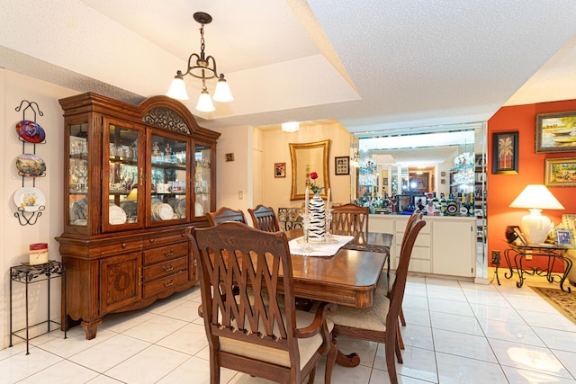 tiled dining area with a raised ceiling, a textured ceiling, and a notable chandelier