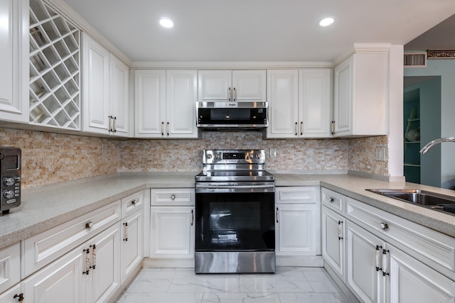 kitchen with white cabinets, backsplash, light tile floors, and stainless steel appliances