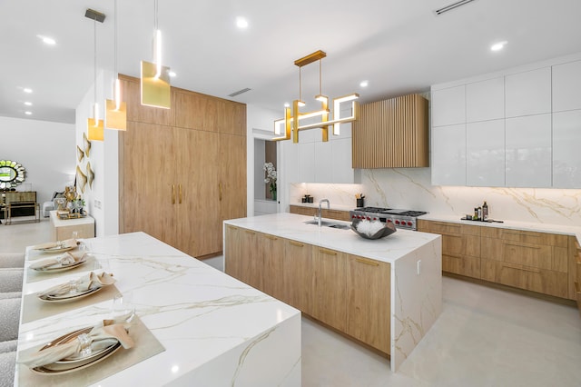 kitchen with backsplash, a center island with sink, light stone counters, pendant lighting, and range with gas cooktop