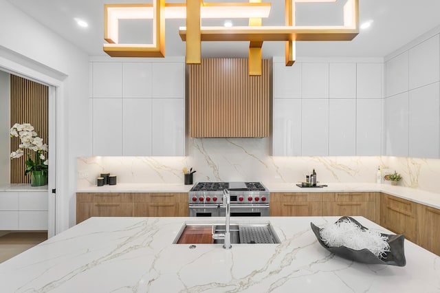 kitchen with light stone countertops, white cabinetry, double oven range, sink, and tasteful backsplash