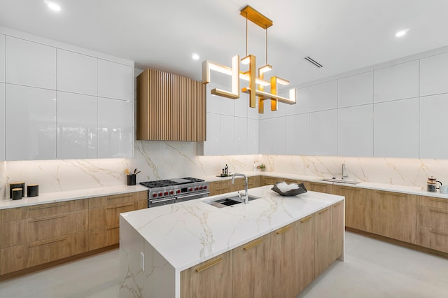 kitchen featuring light stone counters, sink, range with two ovens, hanging light fixtures, and an island with sink