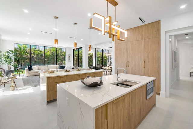 kitchen with sink, decorative light fixtures, a wall of windows, a large island, and light stone countertops