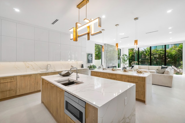 kitchen featuring decorative light fixtures, light stone counters, stainless steel microwave, and a spacious island