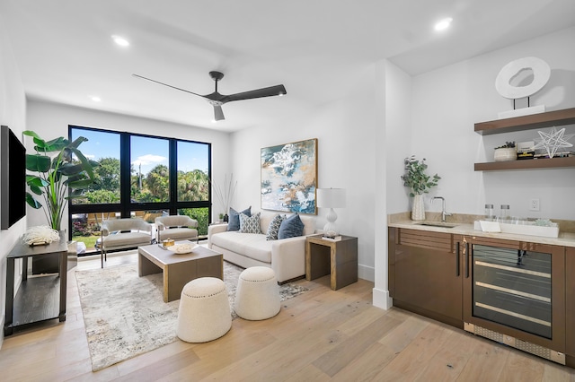 living room with light hardwood / wood-style flooring, ceiling fan, sink, and beverage cooler