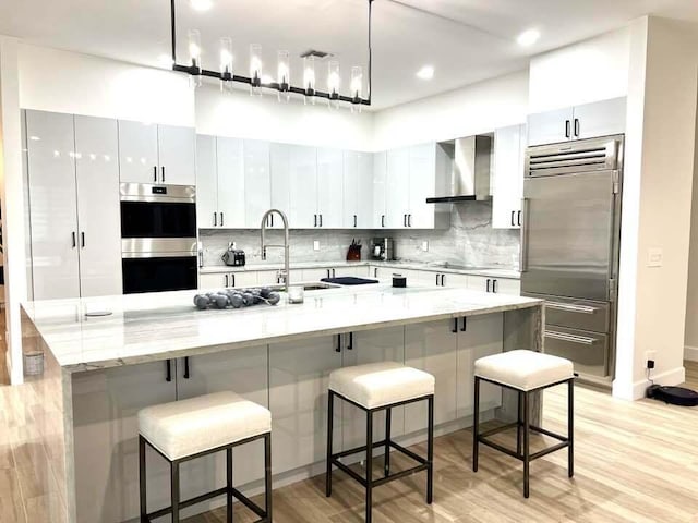 kitchen featuring appliances with stainless steel finishes, a breakfast bar, white cabinetry, and wall chimney exhaust hood