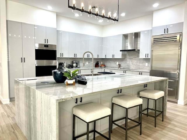 kitchen with pendant lighting, light hardwood / wood-style floors, a kitchen bar, wall chimney range hood, and a spacious island