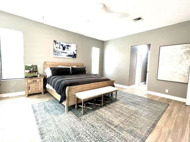 bedroom featuring light wood-style floors, baseboards, visible vents, and ceiling fan