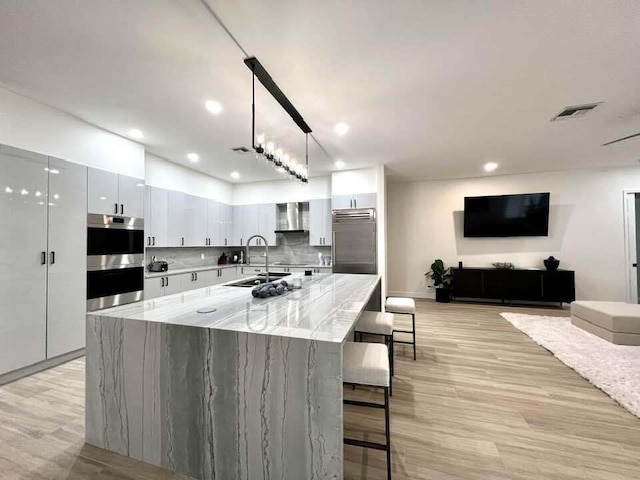 kitchen featuring white cabinets, hanging light fixtures, wall chimney exhaust hood, stainless steel appliances, and a spacious island