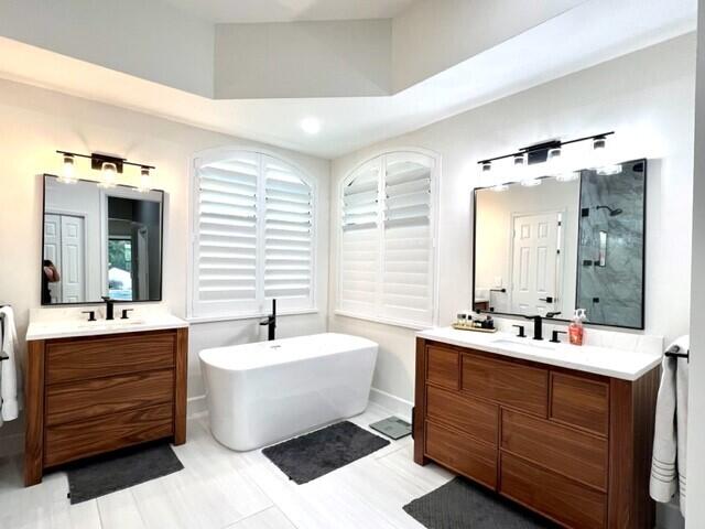 full bath featuring a stall shower, a freestanding tub, two vanities, and a sink