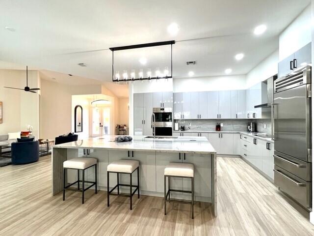 kitchen featuring white cabinetry, stainless steel appliances, a large island with sink, and light countertops