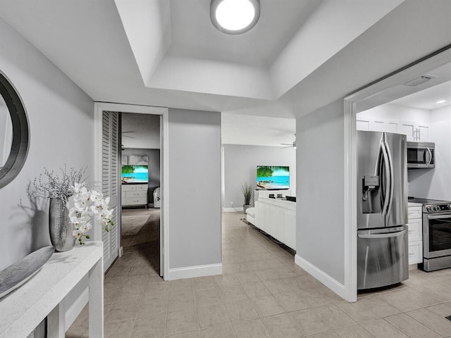 kitchen with ceiling fan, appliances with stainless steel finishes, a tray ceiling, and light tile patterned floors