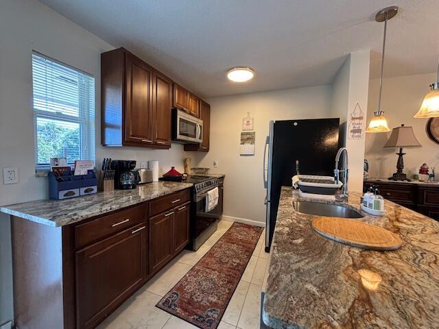 kitchen with dark stone counters, sink, stainless steel appliances, and decorative light fixtures