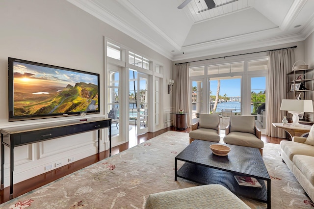 living room with ornamental molding, a water view, hardwood / wood-style floors, a towering ceiling, and a raised ceiling