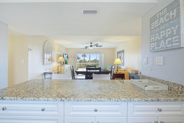 kitchen with open floor plan, light stone countertops, visible vents, and white cabinetry