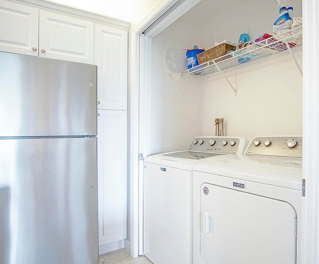 clothes washing area featuring separate washer and dryer, light tile patterned flooring, and cabinet space