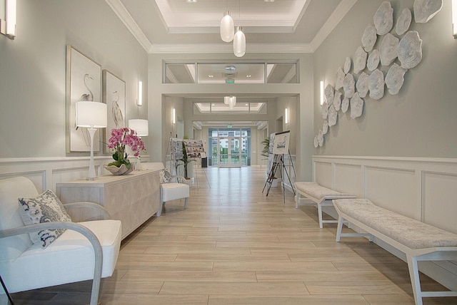 hall with crown molding, a raised ceiling, light wood-style flooring, and a decorative wall