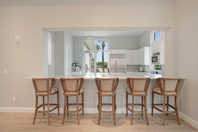 kitchen with light countertops, light wood-style flooring, appliances with stainless steel finishes, white cabinets, and a peninsula