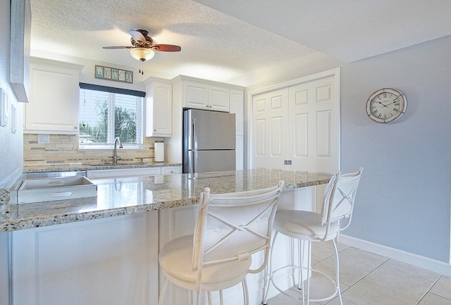 kitchen with light stone counters, stainless steel refrigerator, ceiling fan, and white cabinetry