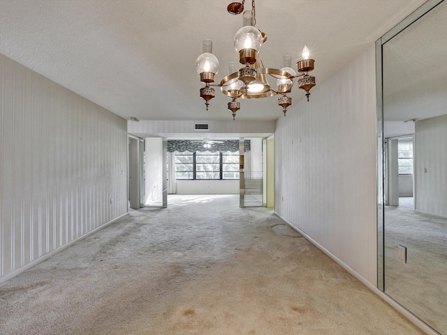 spare room featuring a textured ceiling, carpet, and an inviting chandelier