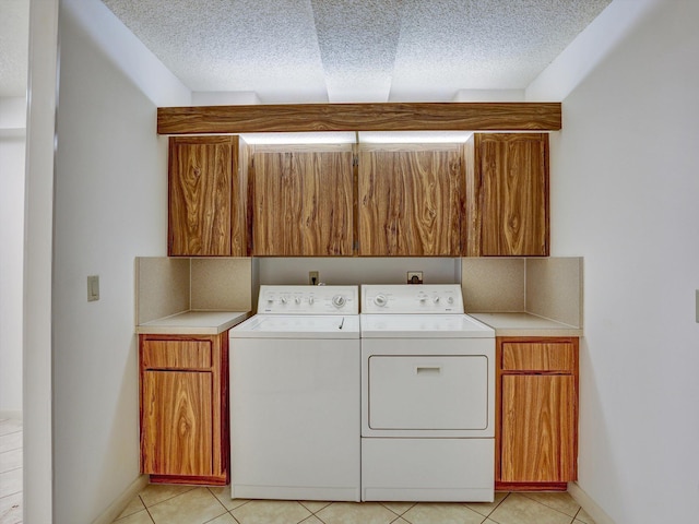 laundry room with washer and clothes dryer, cabinets, a textured ceiling, and light tile flooring