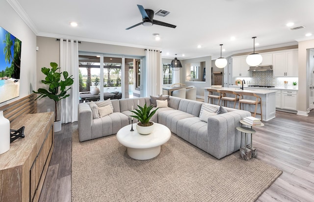 living room with ceiling fan, light wood-type flooring, and ornamental molding