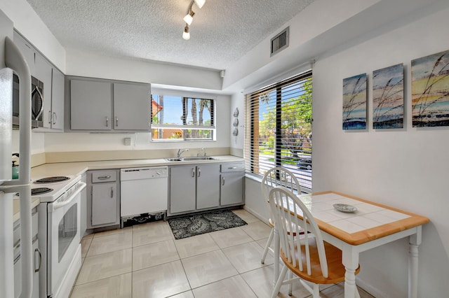 kitchen featuring white appliances, light tile floors, sink, track lighting, and a textured ceiling