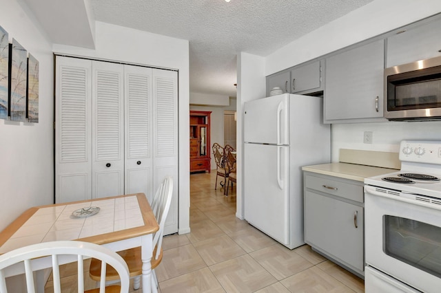 kitchen with gray cabinets, white appliances, a textured ceiling, tile countertops, and light tile floors