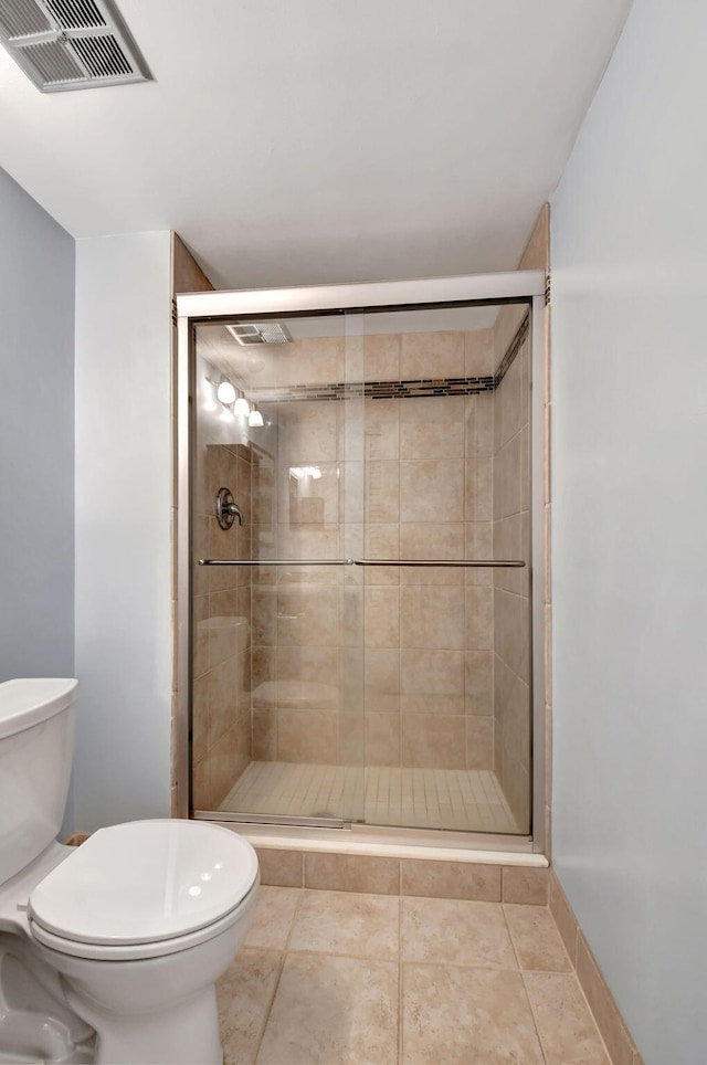 bathroom featuring a shower with shower door, toilet, and tile floors