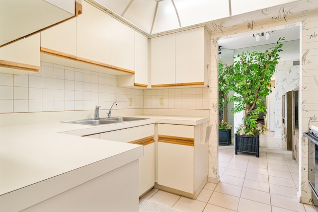 kitchen featuring tile walls, backsplash, white cabinets, sink, and light tile floors