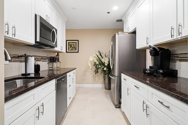 kitchen featuring white cabinets, stainless steel appliances, light tile floors, tasteful backsplash, and dark stone counters