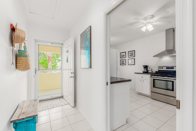 kitchen with white cabinets, light tile flooring, wall chimney range hood, stainless steel electric range oven, and ceiling fan