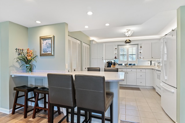 kitchen featuring white cabinets, a breakfast bar area, kitchen peninsula, and white appliances