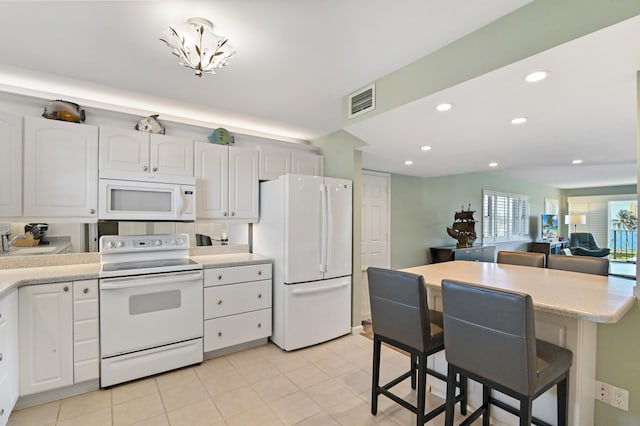 kitchen with white cabinets, white appliances, a kitchen bar, and light tile patterned floors