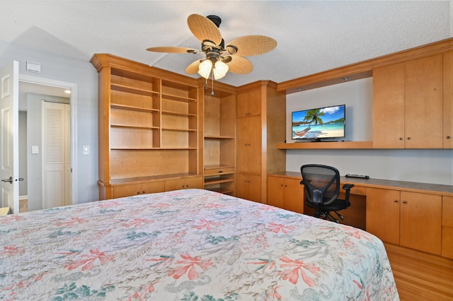 bedroom featuring built in desk, light hardwood / wood-style floors, ceiling fan, and a textured ceiling