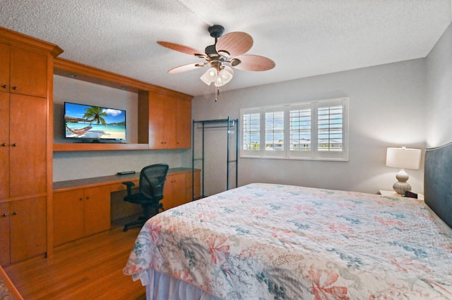 bedroom with light hardwood / wood-style flooring, built in desk, ceiling fan, and a textured ceiling