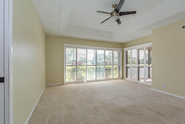 carpeted empty room featuring a textured ceiling, ceiling fan, and a tray ceiling