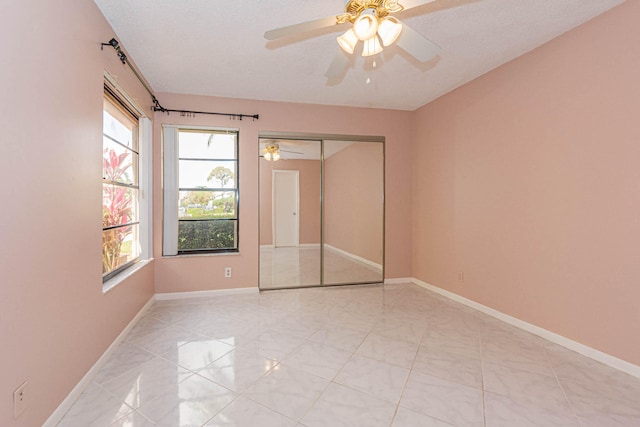 empty room with ceiling fan, light tile flooring, and a textured ceiling