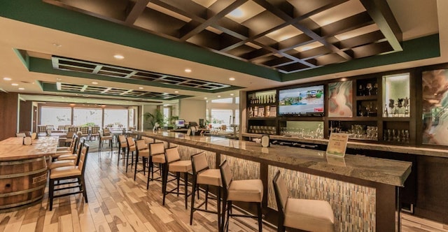 bar with stone countertops, light hardwood / wood-style flooring, and coffered ceiling