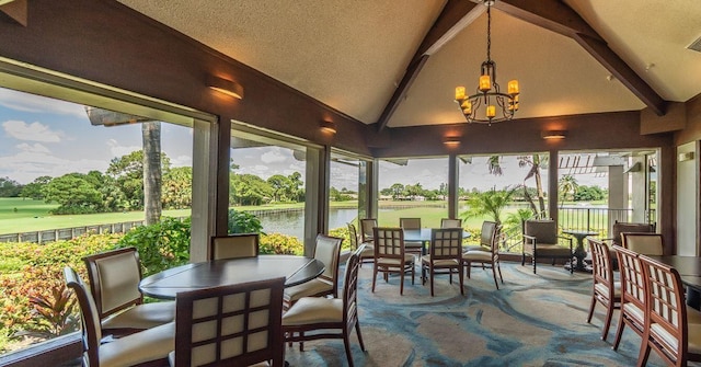 sunroom with an inviting chandelier, vaulted ceiling with beams, and a water view