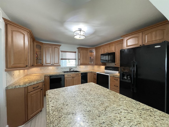 kitchen featuring black appliances, decorative backsplash, light stone counters, and sink