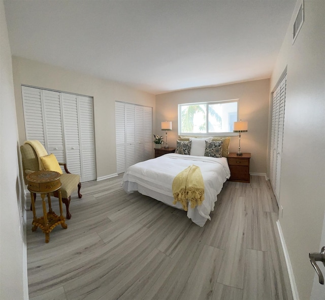 bedroom with two closets and light hardwood / wood-style flooring