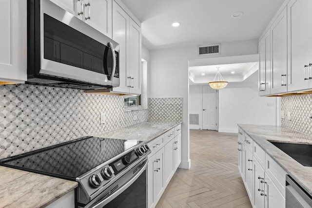 kitchen with stainless steel appliances, white cabinets, light parquet flooring, and backsplash