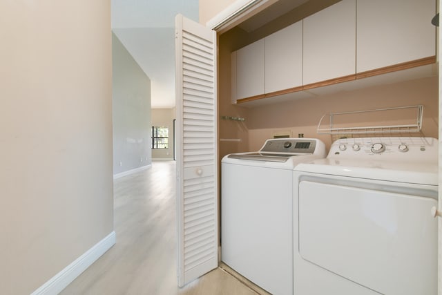 clothes washing area with cabinets, light wood-type flooring, and washing machine and clothes dryer