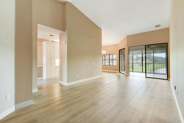 spare room with a chandelier, a towering ceiling, and light hardwood / wood-style flooring