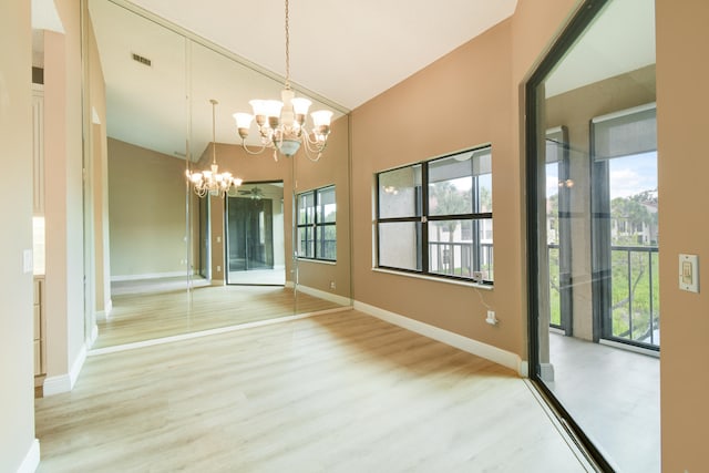 unfurnished dining area featuring hardwood / wood-style floors, vaulted ceiling, an inviting chandelier, and plenty of natural light