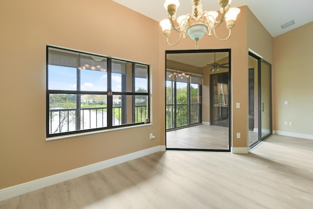 empty room with a water view, wood-type flooring, and ceiling fan with notable chandelier