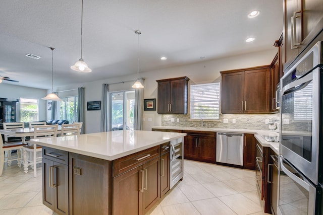 kitchen with a center island, hanging light fixtures, decorative backsplash, stainless steel appliances, and ceiling fan