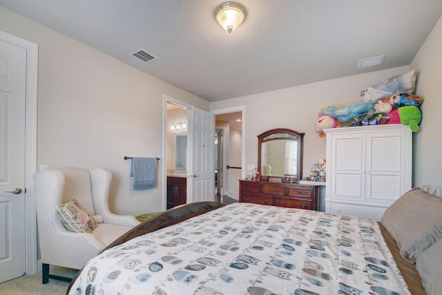 bedroom with a textured ceiling, ensuite bath, and carpet