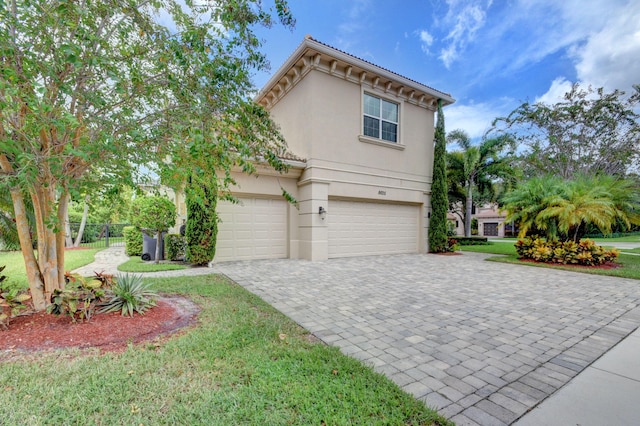 view of front of home featuring an attached garage, fence, decorative driveway, a front lawn, and stucco siding